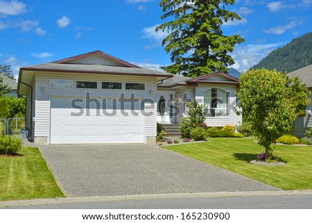 Average family house with concrete driveway, wide garage door, and blue sky background.