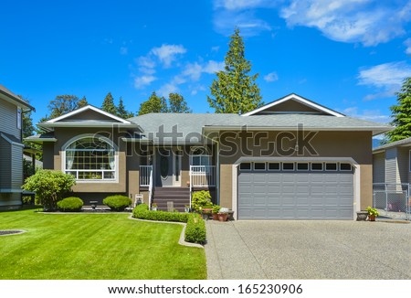 Suburban family house with concrete driveway, wide garage door on blue sky background.