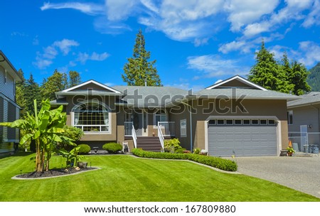 Suburban family house with concrete driveway, wide garage door on blue sky background. Family house with a palm tree on front and cloudy sky background.