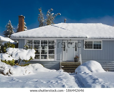 Family house with looking through window in the living room. Residential house in snow on a sunny day. Grey house at winter season on blue sky background.