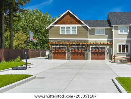 Fragment of brand new farmer\'s house with three garage doors and concrete driveway in front and blue sky background. Basketball ring in front of huge farmer\'s house.