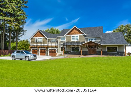 Brand new farmer\'s house with car parked on driveway in front. Huge family house with three garage door and blue sky background. British Columbia, Canada.