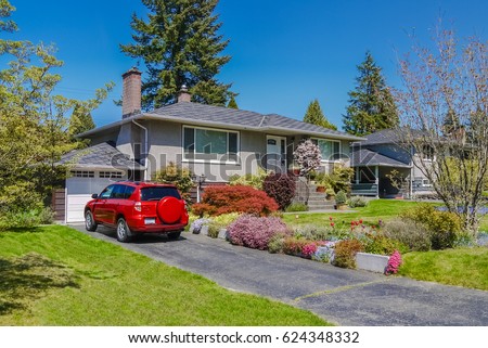 Modest residential house with red car parked on driveway in front. Family house with blossoming flowers on the front yard