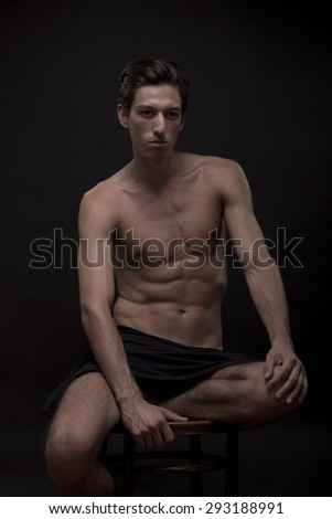 Skinny male model posing, clean black background.