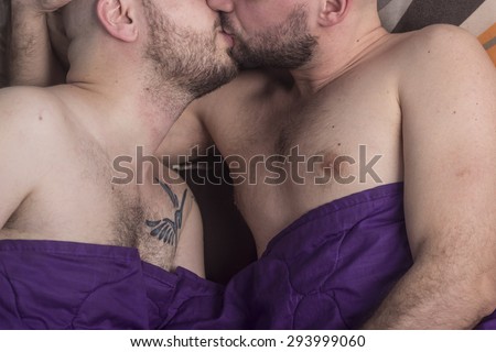 Gay couple kissing in bed, covered with bed sheet.