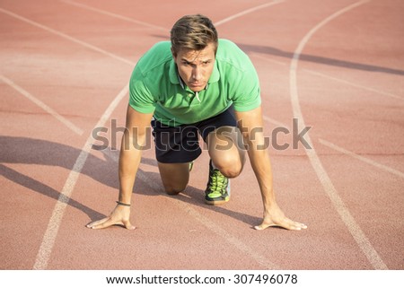 Male sprinter in clothes at start position, on red track.