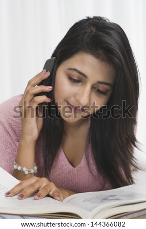 Woman reading a book while talking on a mobile phone