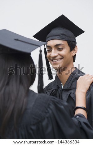 Man in graduation gown looking at a woman and smiling