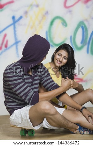 Couple sitting with a skateboard in front of a graffiti covered wall