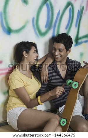 Couple sitting with a skateboard in front of a graffiti covered wall