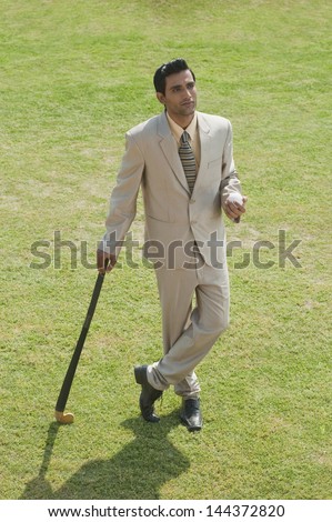 Businessman holding a hockey stick and a ball in a field
