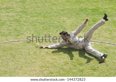 Businessman diving to stop a ball near boundary line in a cricket field