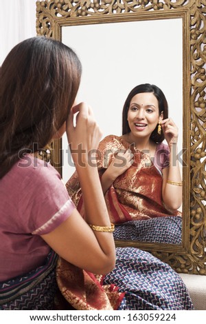 Reflection of a woman in mirror trying a sari and earring on herself