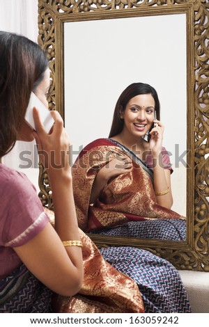 Reflection of a woman in mirror trying a sari on herself and talking on a mobile phone