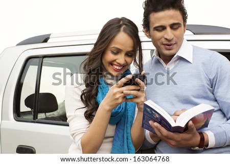 Woman text messaging with a mobile phone and man reading a book
