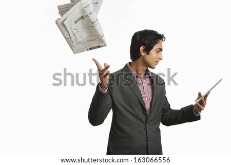 Businessman looking at a digital tablet and throwing newspaper
