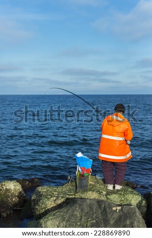 Fisherman in orange wind coat fishing on the shore of Black Sea