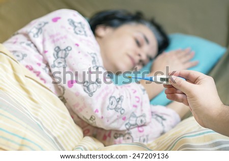 Holding thermometer over an ill woman with high fever laying in bed