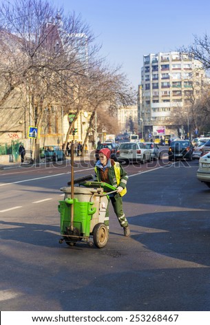 BUCHAREST, ROMANIA - FEBRUARY 14, 2015: Woman street worker pushing a cleaning trolley in daylight on the street