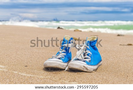 Blue pair of worn sneakers on beach sand in summer day with sea in background