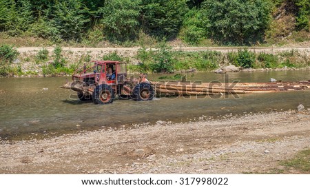VISEUL DE SUS, ROMANIA - AUGUST 10, 2015: Rusty tractor transporting cut wood along river Valea Vaserului in Maramures county during summer season when water level is not very high