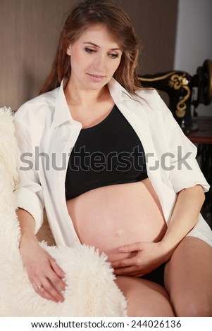 Pregnant woman in white shirt holding her belly