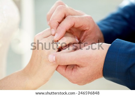 Groom is putting on a ring on bride\'s finger