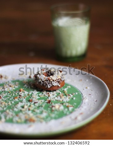 Donut with coconut and chopped hazelnuts on plate and a glass of milk
