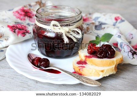 Sweet cherry jam with whole cherries and walnuts in a jar and wheat toasts with jam on a plate for breakfast