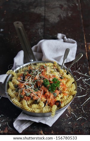 Italian fusilli pasta dish with tuna fish fillet, tomato sauce, capers and cheese in a pan