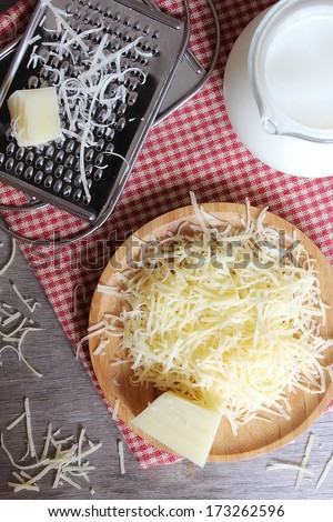 Freshly grated parmesan and cheddar cheese on a wooden board and grater and fresh milk pot
