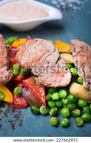 Roasted pork fillet meat with frozen peas, red belle pepper, zucchini, eggplant with cream sauce on a plate