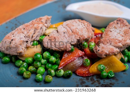 Roasted pork meat fillet chops with zucchini, onion, bell pepper, frozen peas on a plate with cream sauce