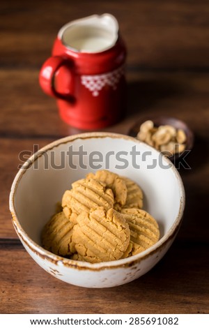 Peanut butter cookies in a bowl with a pot of fresh milk and a small bowl of peanuts, selective focus