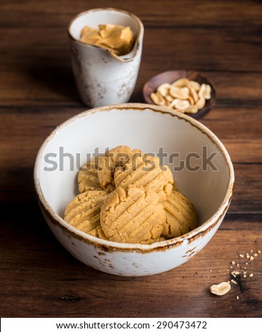 Peanut butter cookies with nuts and chocolate chunks and a cup of peanut butter and a small wooden plate with toasted peanuts, selective focus