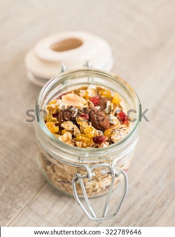 Homemade granola with oat flakes, toasted almonds, peanuts, dried cranberry, goji berries in a jar on a wooden rustic table, selective focus
