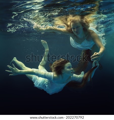 Woman and girl in beautiful dresses swim underwater.