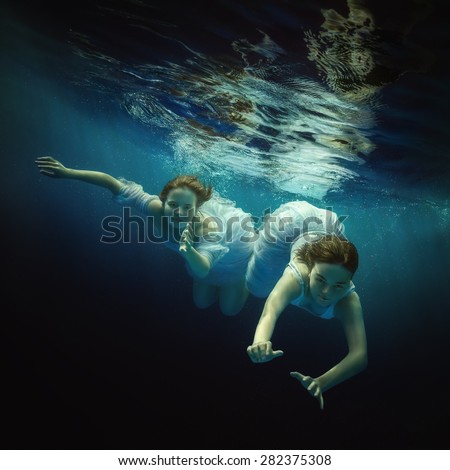 Two girls swim underwater.