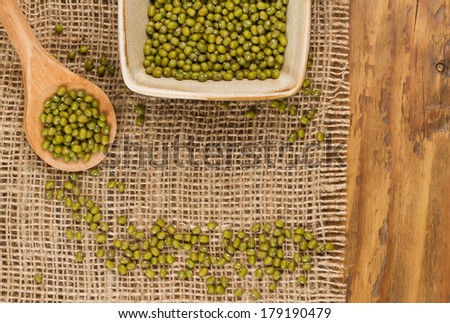 Mung beans in wooden spoon and bowl with mung beans on burlap