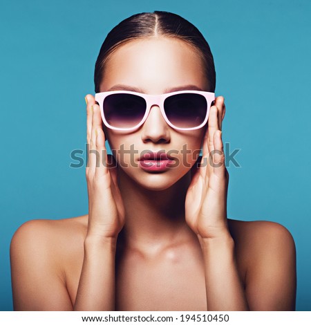 Portrait of a beautiful young girl in sunglasses on a blue background