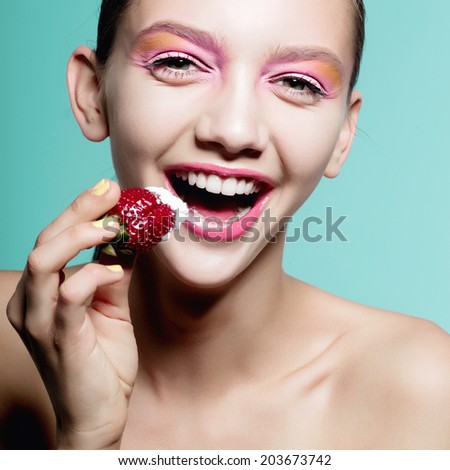 Close up of girl with brilliant pink make-up eating strawberry. Concept of beauty and healthy food, blue background.