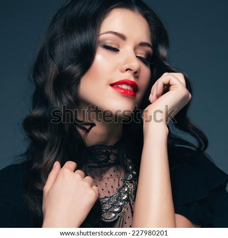 Portrait of a beautiful girl in a black dress and red lipstick with eyes closed, posing in studio on dark background