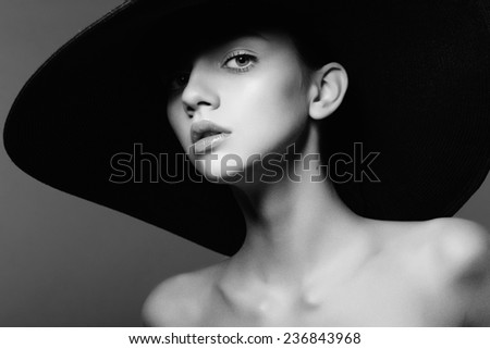 Portrait of a beautiful young girl in a hat, black and white photography in the studio