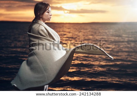 Portrait of a beautiful brunette girl in a coat on a background of the sea and the sunset, the wind blows her hair