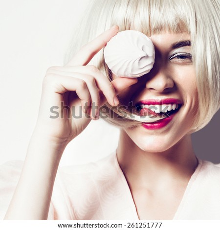 Portrait of a beautiful happy young blonde girl in the studio on a white background with marshmallow in hand