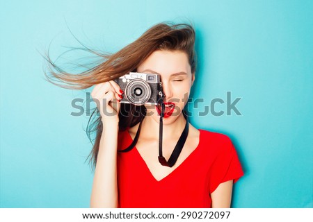 Expressive portrait of a beautiful young brunette woman in a red dress in the studio on a blue background with a camera in his hands