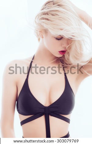 Portrait of a beautiful young blonde girl with long hair in a black bathing suit in the studio on a white background, the concept of beauty