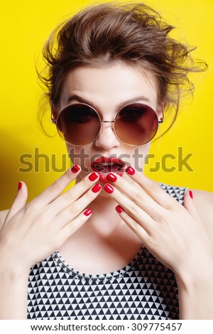 Portrait of a beautiful girl in round glasses on a yellow background in the studio posing surprise