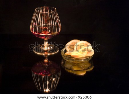glass of fine cognac with lemon slices on black background reflected