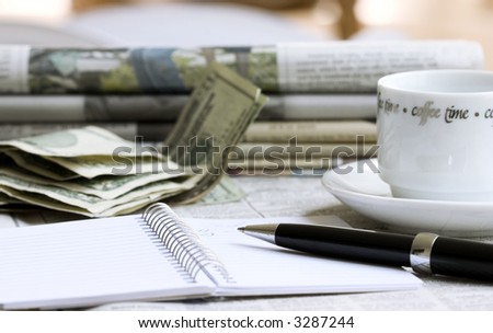 Notebook with pen, money, newspapers and cup of coffee